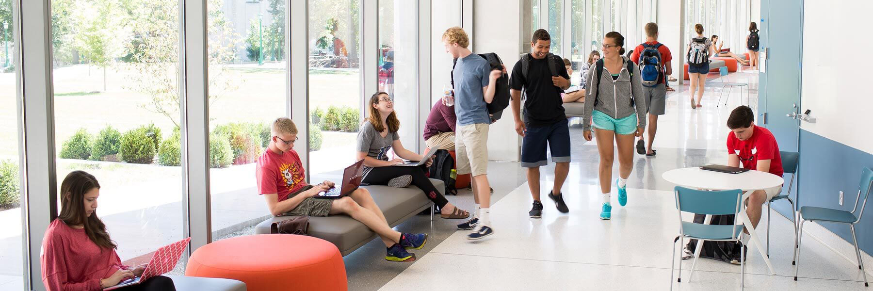 Groups of students studying on benches and chairs while other students are walking through the hallway